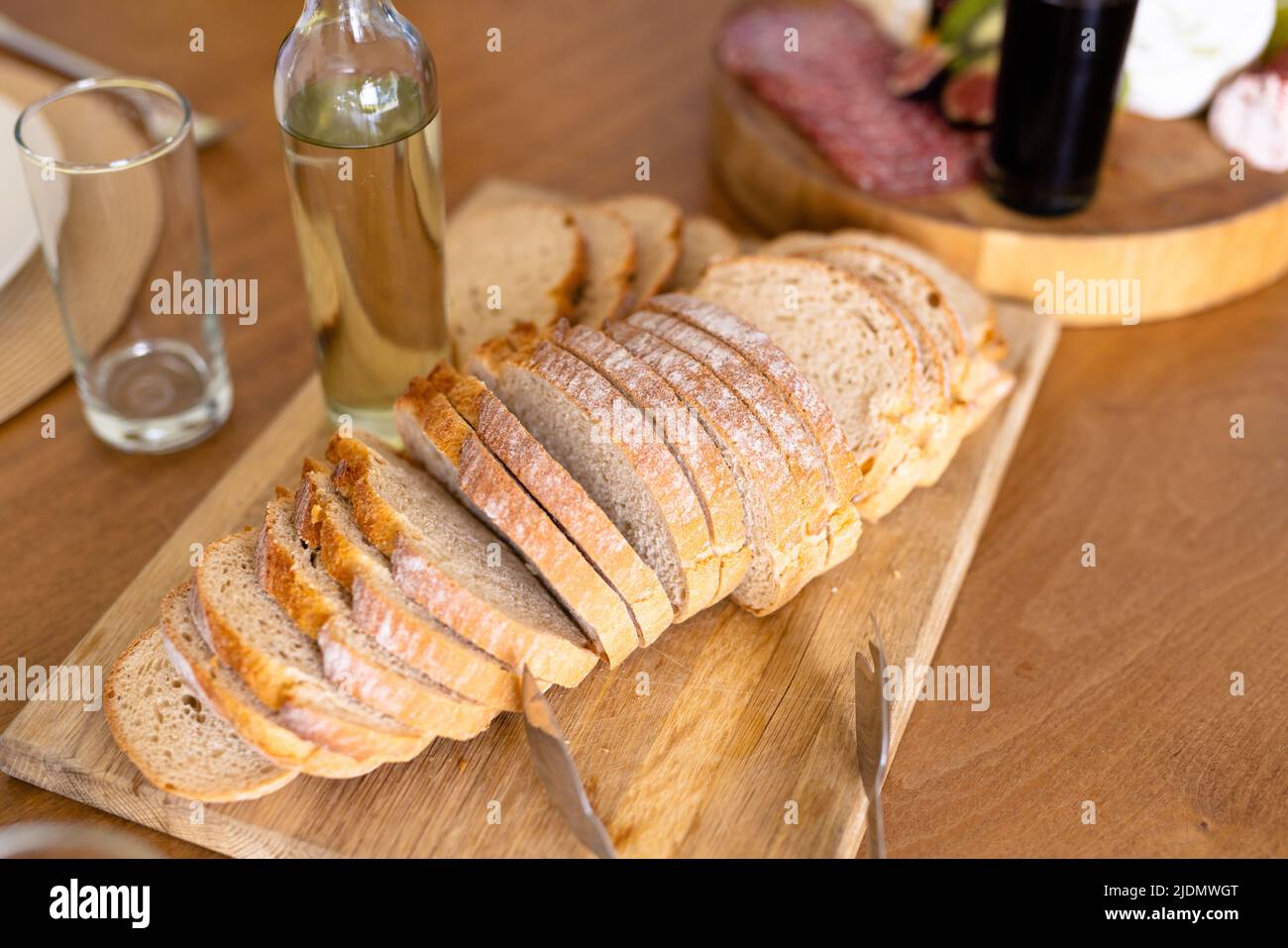 Blick auf Brotscheiben, die an Bord serviert werden, mit einer Trinkflasche und einem Glas auf dem Esstisch Stockfoto