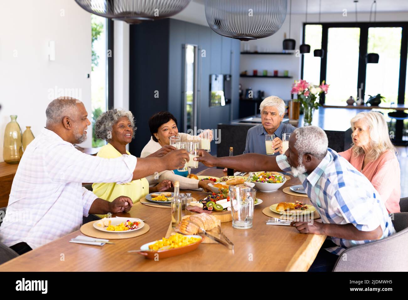Fröhliche, multirassische männliche, weibliche ältere Freunde, die beim Mittagessen am Esstisch Getränke toasten Stockfoto
