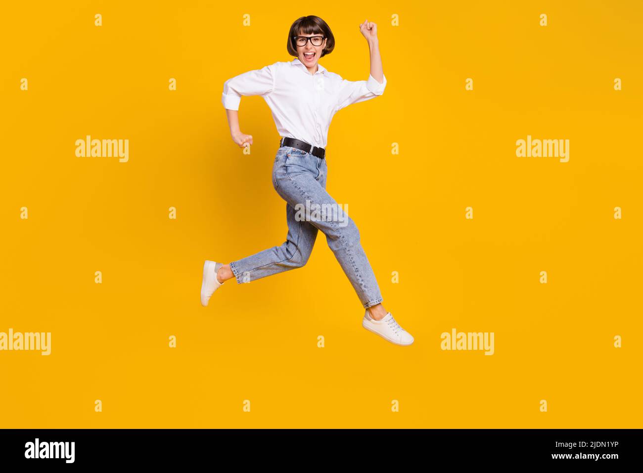 Foto von positiven Glück lustige Dame jump run tragen Brille weißes Hemd  Jeans Schuhe isoliert gelbe Farbe Hintergrund Stockfotografie - Alamy