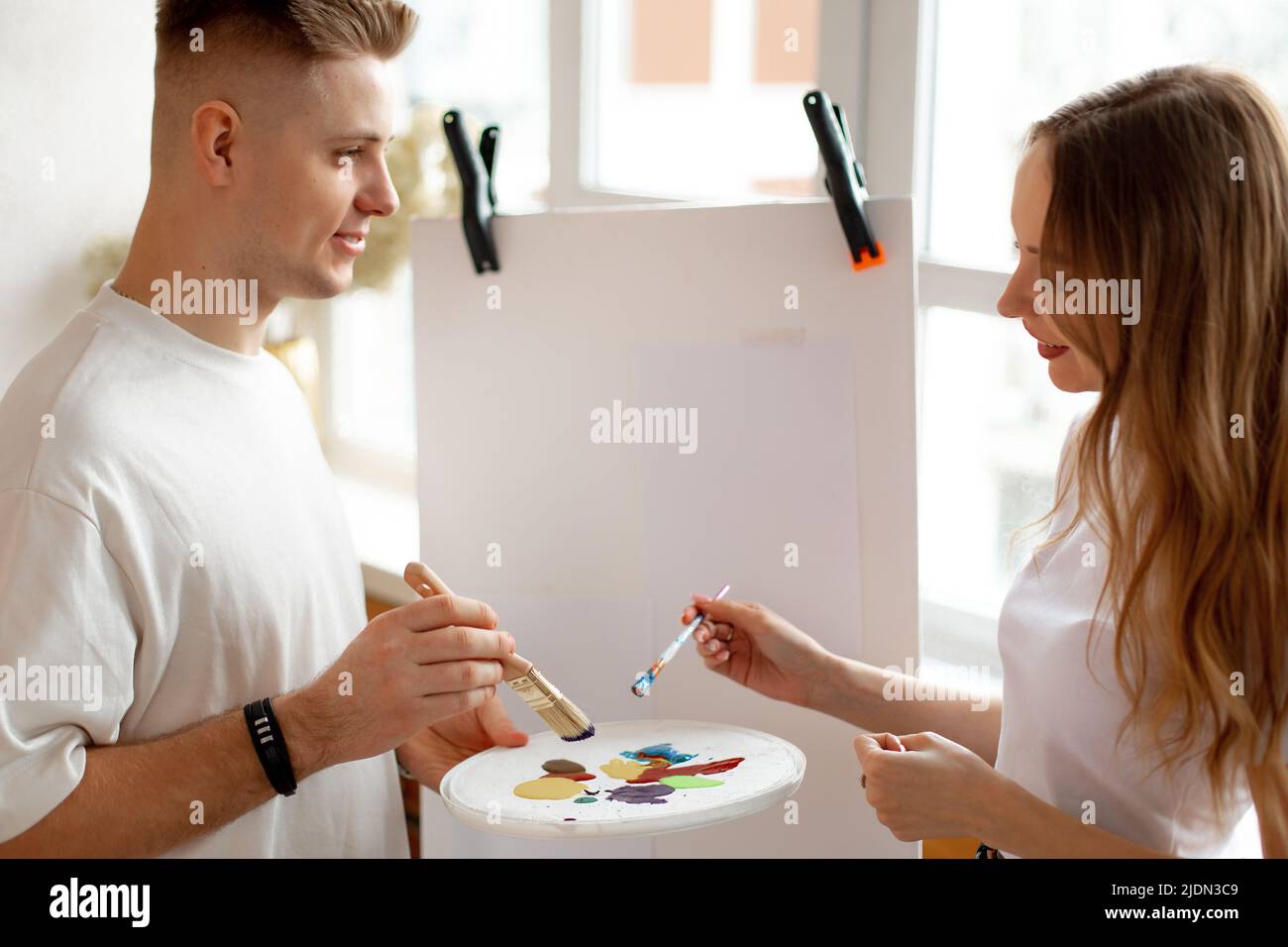 Verheiratetes Paar, das sich zusammenzieht. Frau und Mann malen auf Leinwand und halten Pinsel und Pallette mit Farben. Stockfoto