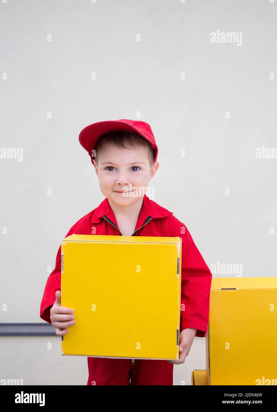 Junge 3-4 Jahre alt in einer roten Uniform und Kappe mit einem gelben Karton in den Händen. express Lieferung von Glück. Positives Feedback. Platz für adver Stockfoto