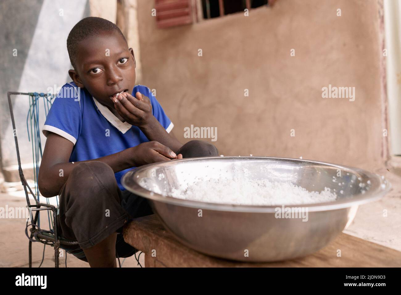 Armer afrikanischer Junge, der einfachen Reis ohne Gewürze, Gemüse oder Fleisch aus einer großen Metallschüssel isst; Konzept der Unterernährung Stockfoto