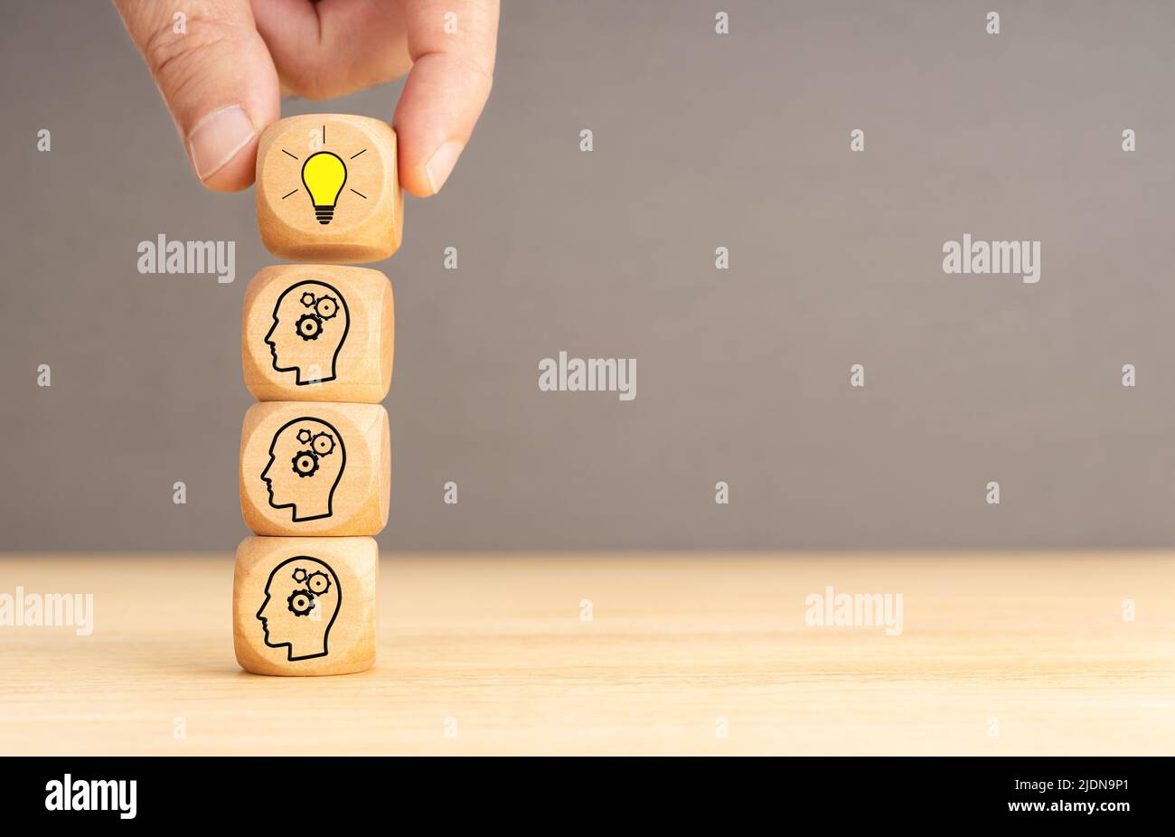 Brainstorming-Prozess und Ideenkonzept. Holzblöcke mit Zahnradsymbol gestapelt und menschliche Hand hält die obere mit Glühbirne Stockfoto