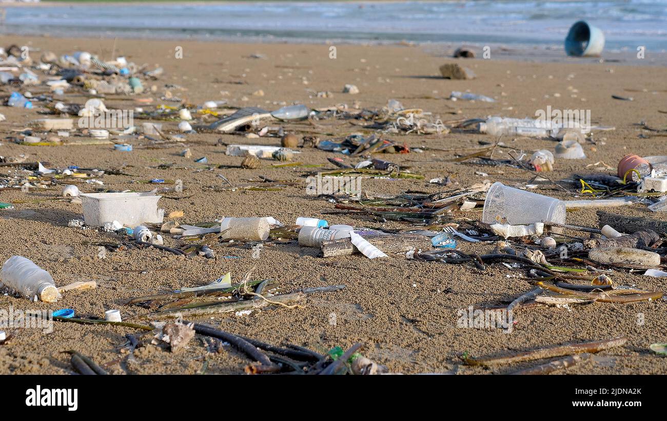 Plastikverschmutzung am Meeresstrand. Abfall bei Flut mit Meereswellen im Hintergrund. Umwelt- und Meeresplastik-Verschmutzung. Verschiedene Arten Stockfoto