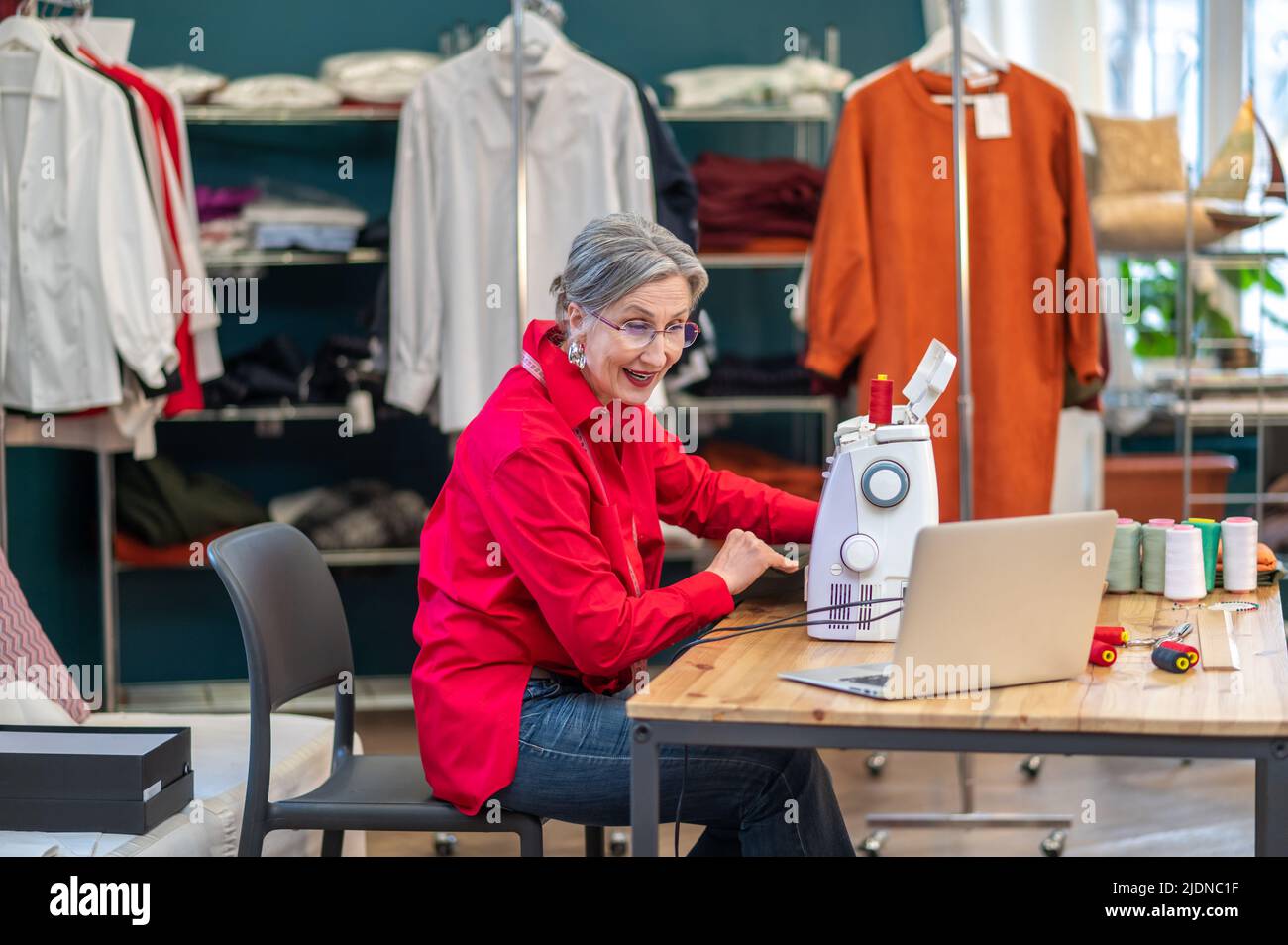 Frau an der Nähmaschine spricht am Laptop-Bildschirm Stockfoto