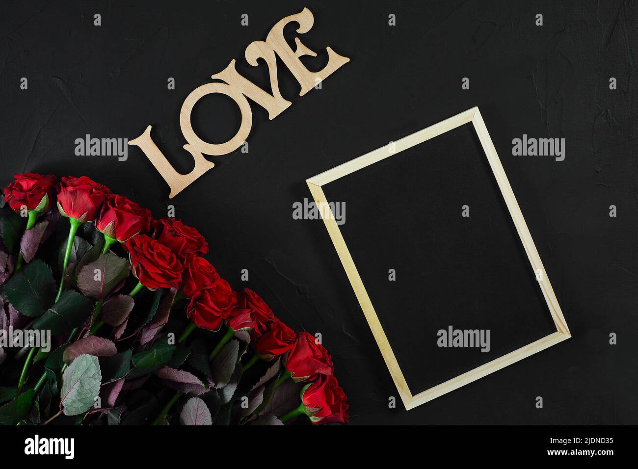 Rote Rosen Blumen mit Holz- Wort LIEBE auf schwarzen Hintergrund mit Stockfoto