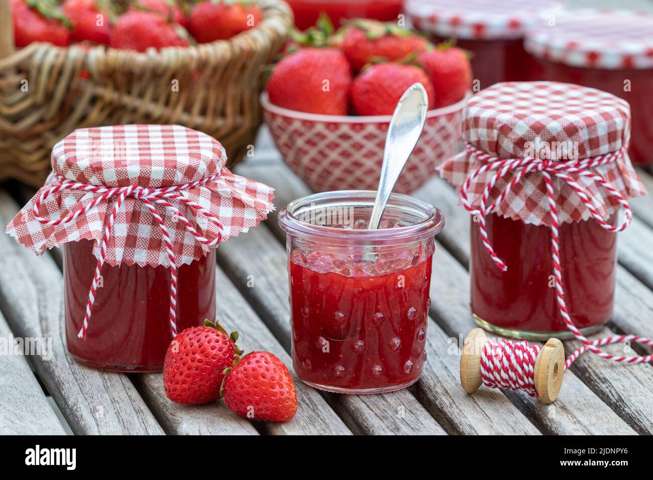 Erdbeermarmelade in Gläsern und frische Erdbeeren in Korb und Schüssel Stockfoto