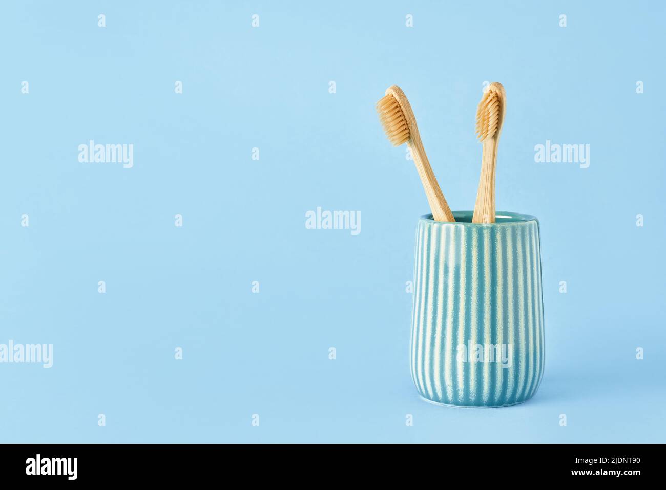 Zwei Bambuszahnbürsten in einem Keramikhalter auf blauem Hintergrund. Umweltfreundliches, abfallfreundliches Konzept. Platz für Text kopieren, selektiver Fokus Stockfoto