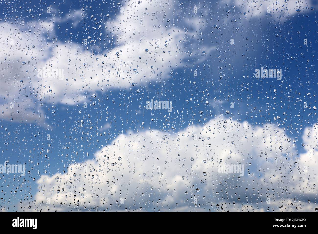 Regentropfen auf dem Glasfenster auf verschwommenem Hintergrund des Himmels mit weißen Wolken. Schöne Wassertropfen, Wetter nach Regen Stockfoto