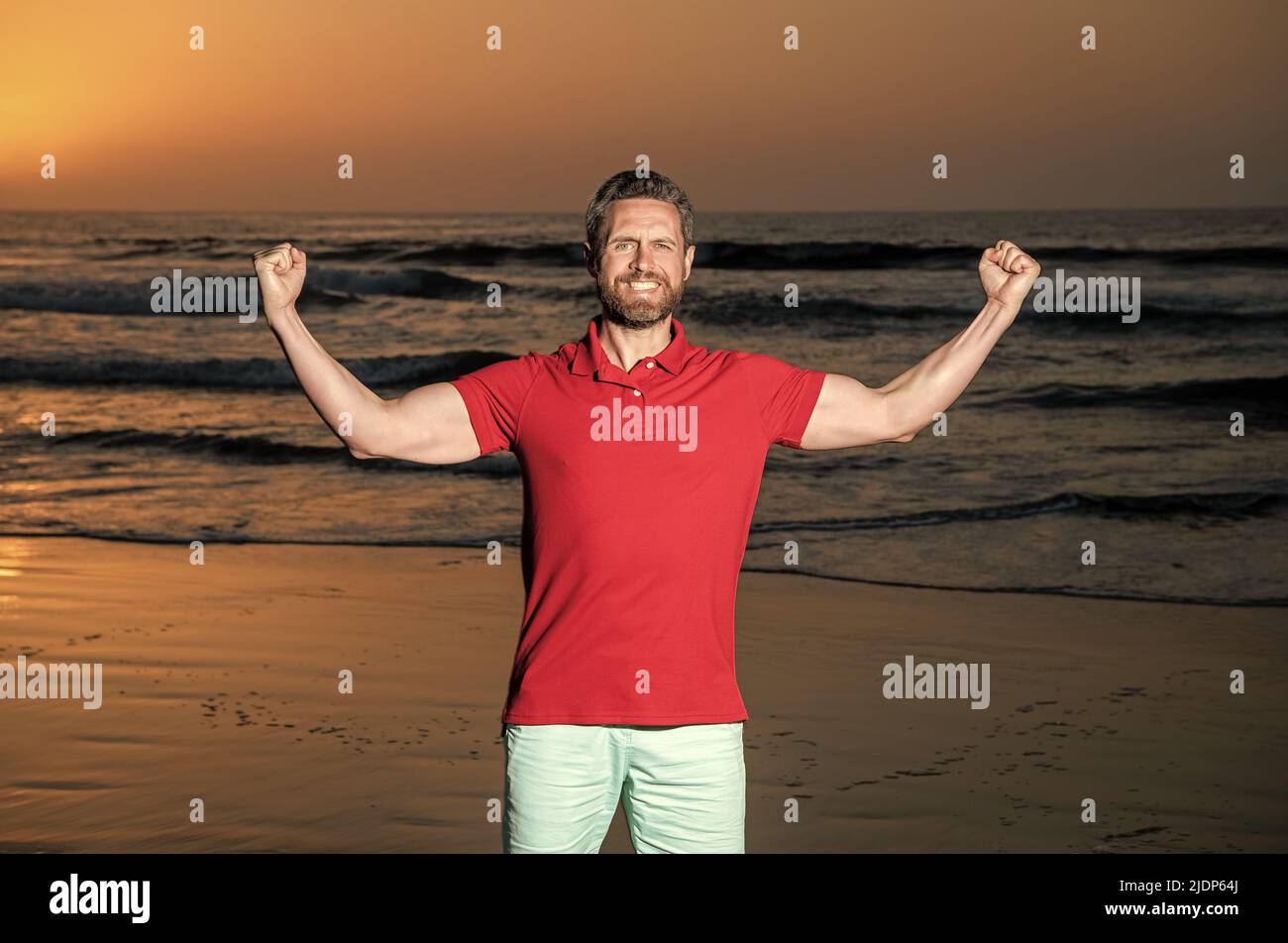 Erfolgreicher Kerl am Strand. kaukasischer Kerl am Sonnenaufgangsstrand. Bärtiger Mann im Hemd. Stockfoto