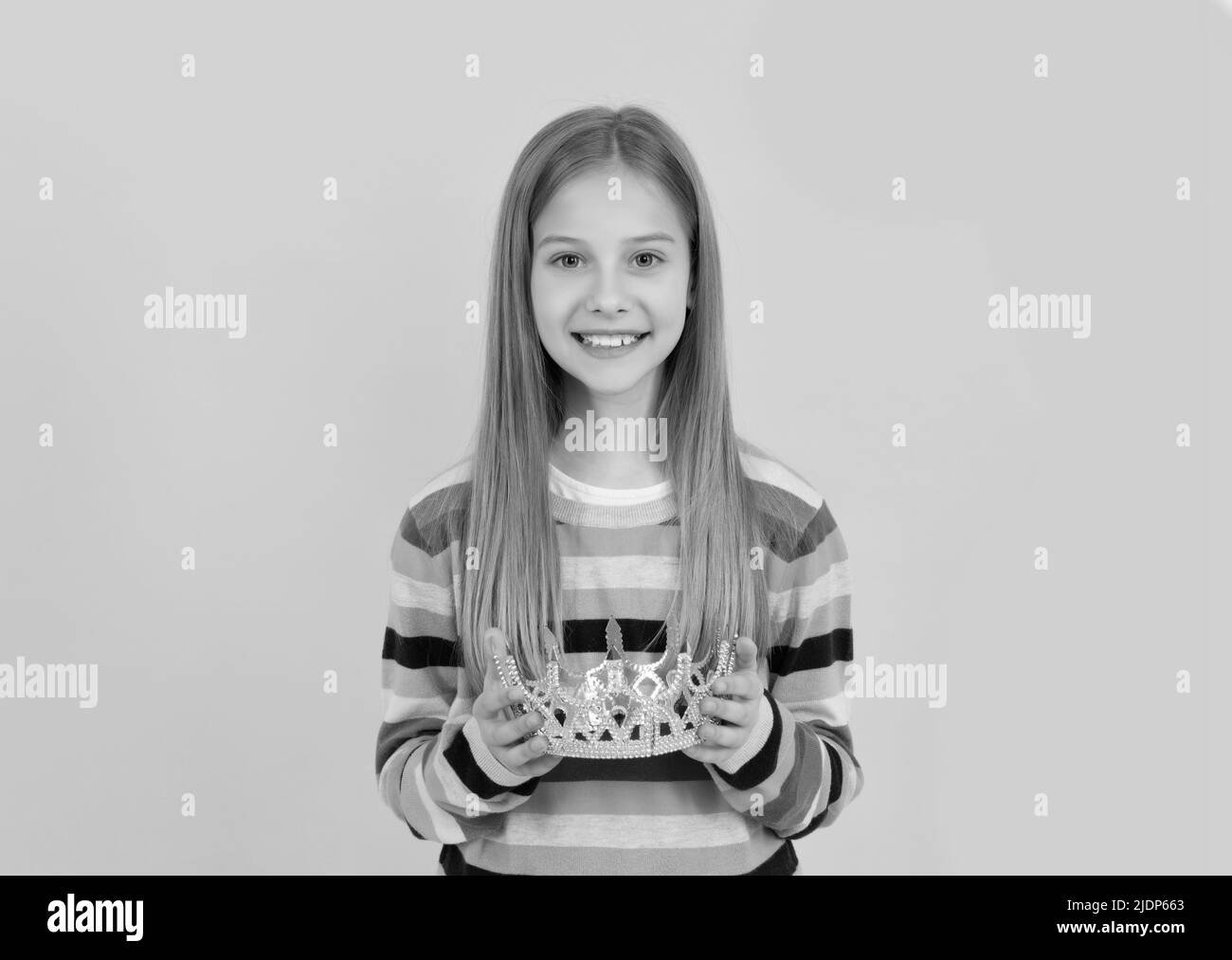 Positive Teenager Kind halten Königin Krone auf gelbem Hintergrund Stockfoto