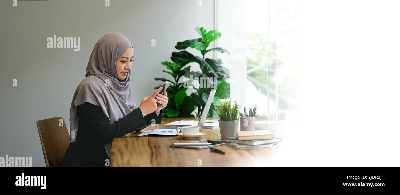 Muslimische asiatische Frau mit Mobiltelefon und Laptop-Computer im modernen Büro. Stockfoto