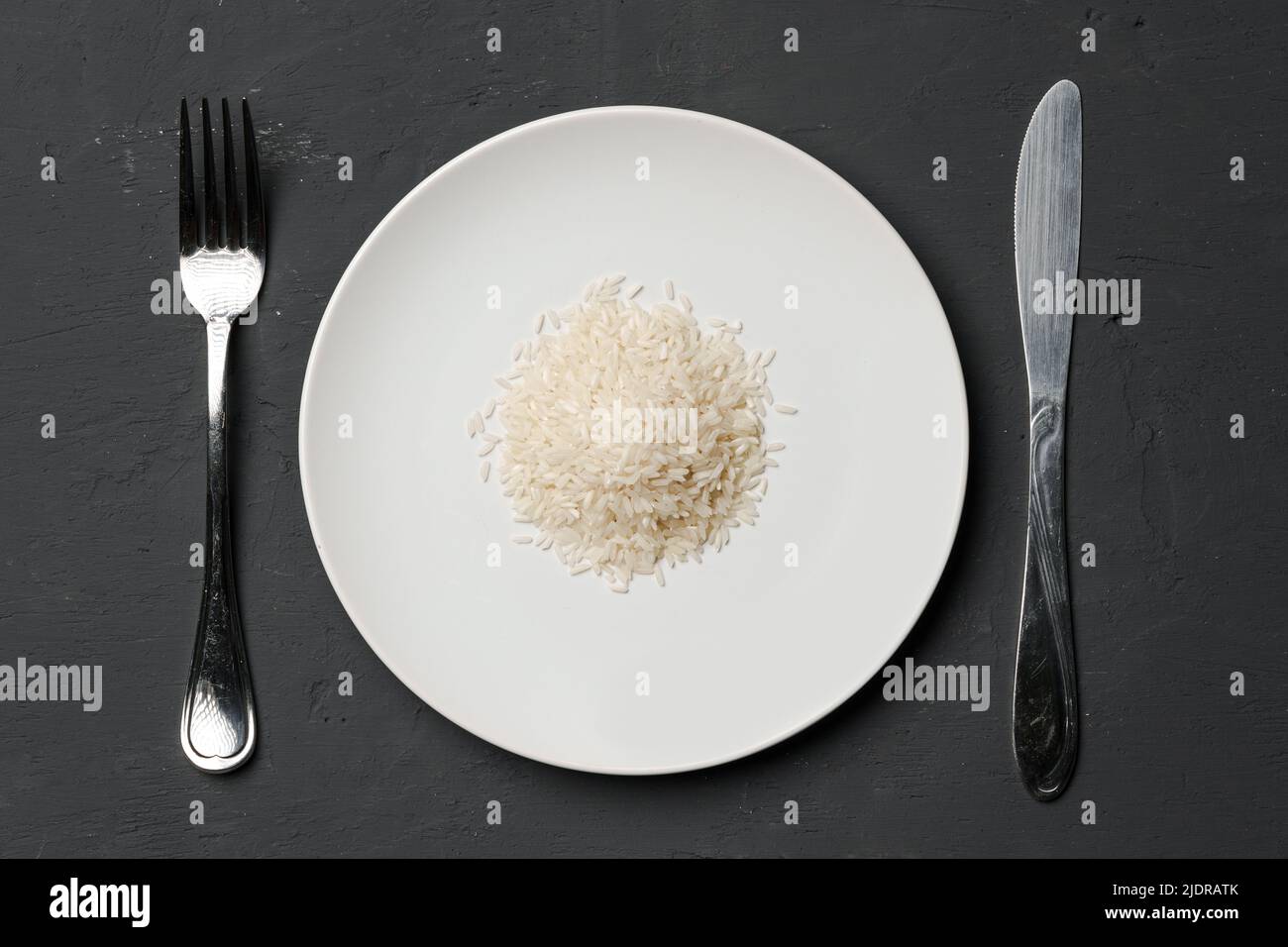 Haufen von trockenem Reis in einer Schüssel auf schwarzem Hintergrund, Mangel an Nahrung, Hunger-Konzept Stockfoto