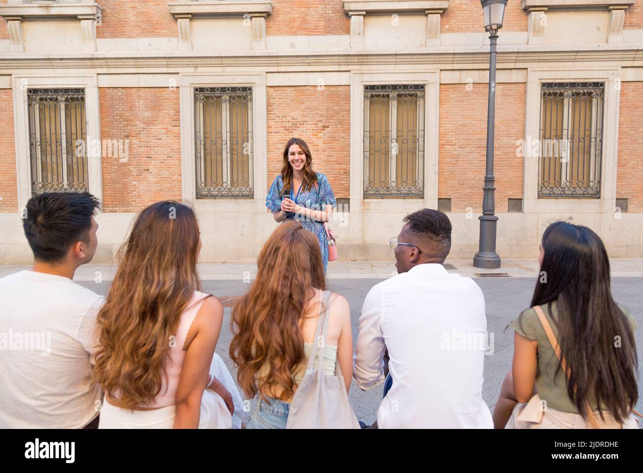 Lächelnde Frau im Sommerkleid, die draußen vor einer Gruppe multiethnischer Freunde spricht Stockfoto