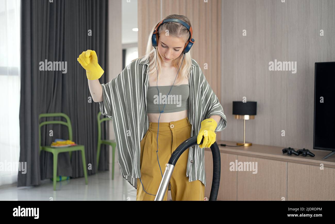 Junges Mädchen havig Spaß beim Reinigen des Bodens mit Staubsauger. Fröhliche Frau, die zu Hause Hausarbeit macht Genießen Sie Musik mit Kopfhörern. Stockfoto