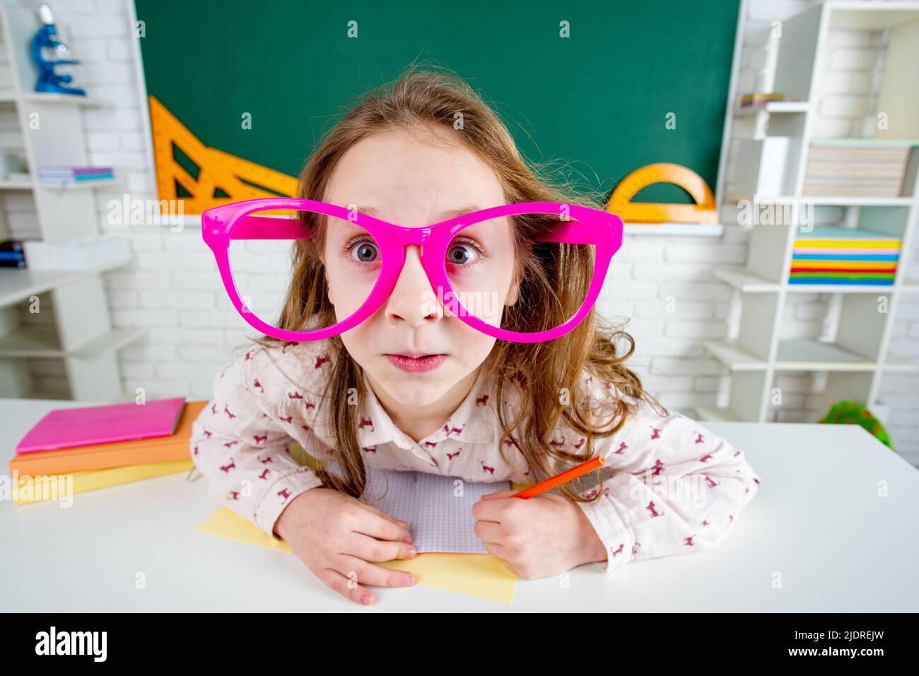 Lustig überrascht Kind Schulmädchen mit Spaß Brille im Klassenzimmer. Stockfoto