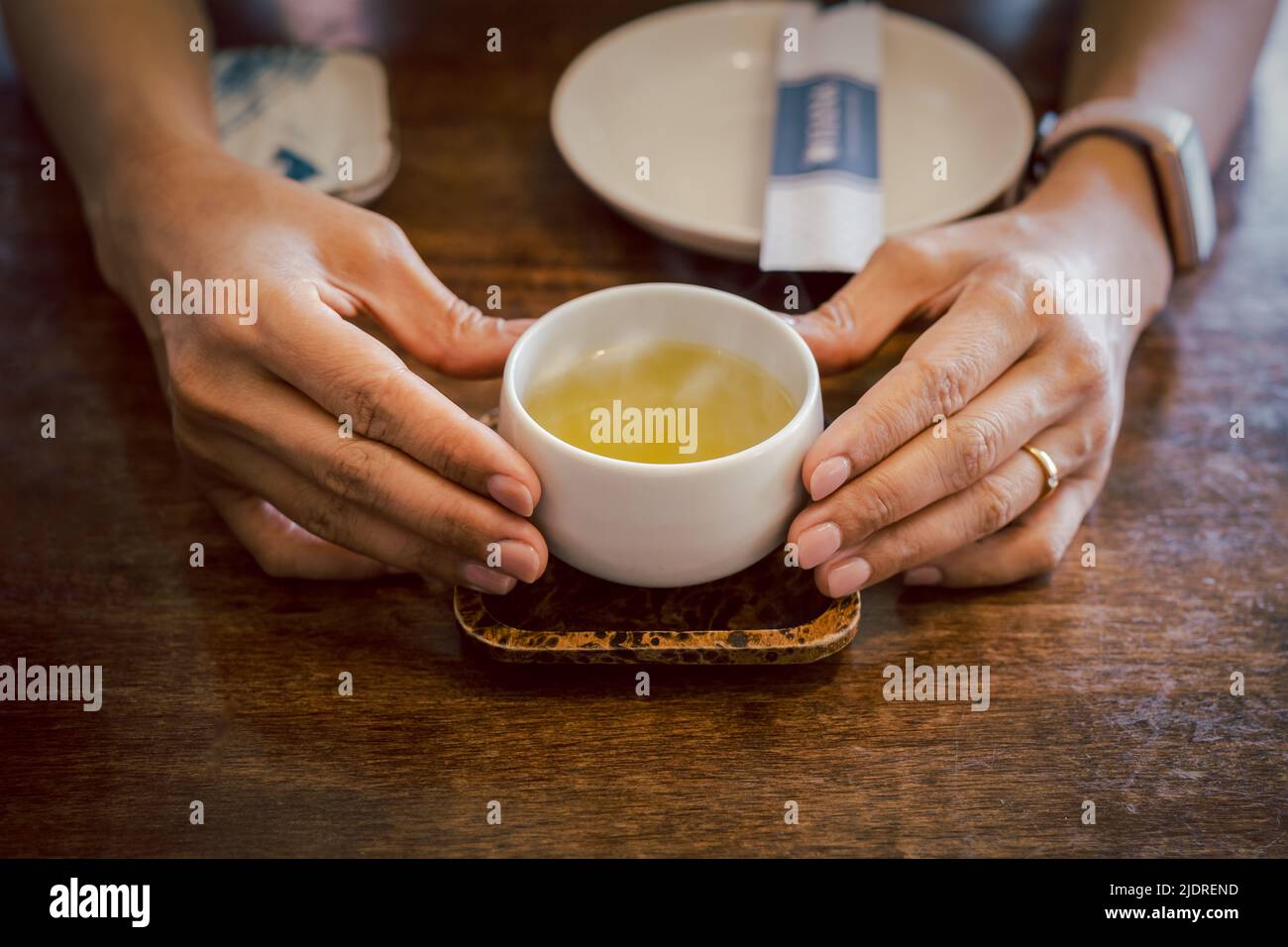 Hände halten Tasse heißen grünen Tee auf einem Tablett Stockfoto