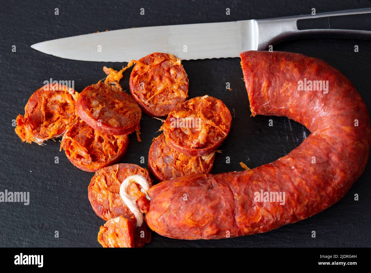 Spanischer Chorizo wurde mit einem Messer auf einem Schieferschneidebrett geschnitten. Stockfoto