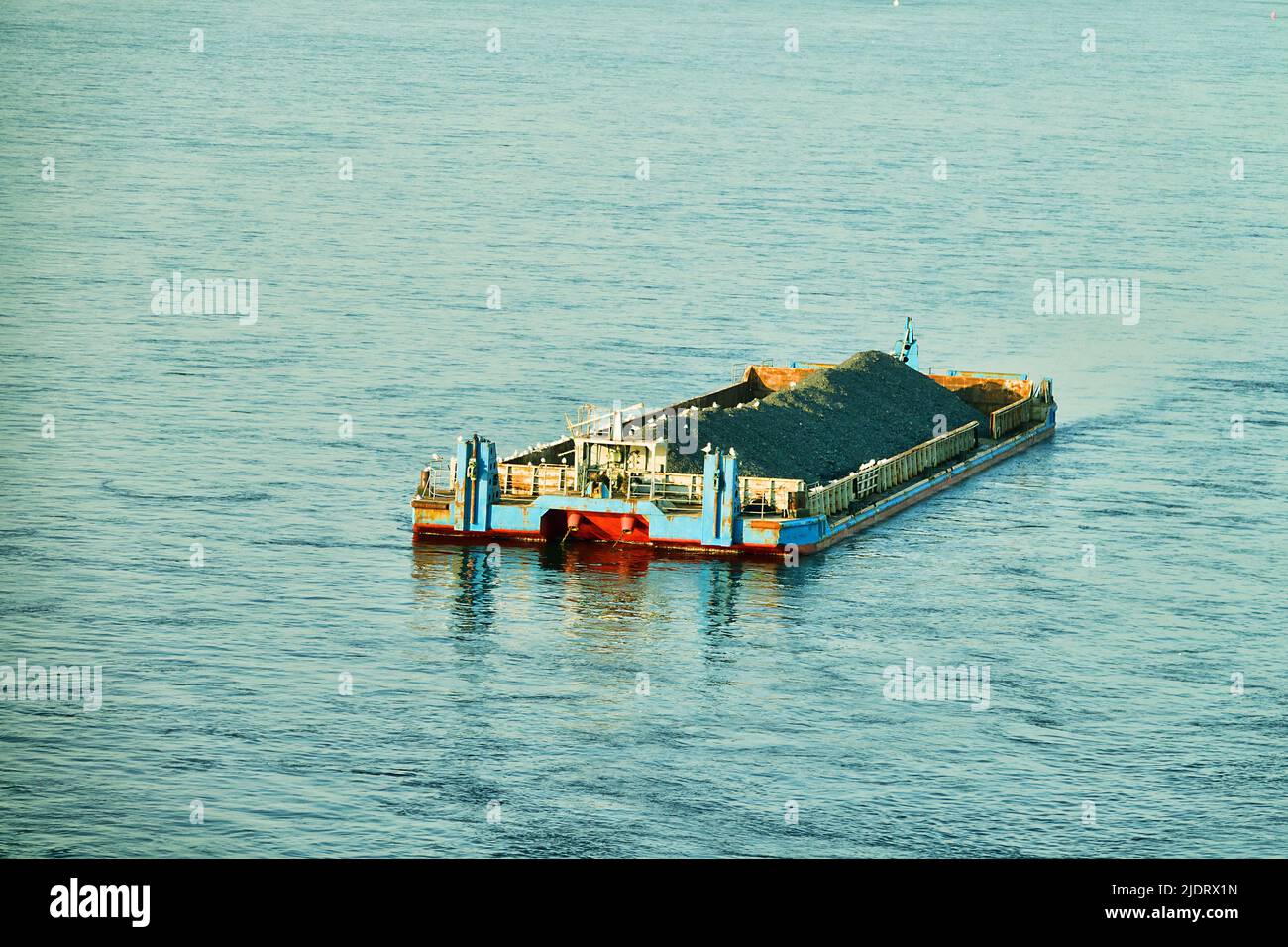 In der Mitte des Flusses ist ein nicht angetriebenes Binnenschiff (Side Stone Dump Vessel) mit Schutt verankert, das auf einen Schlepper wartet Stockfoto