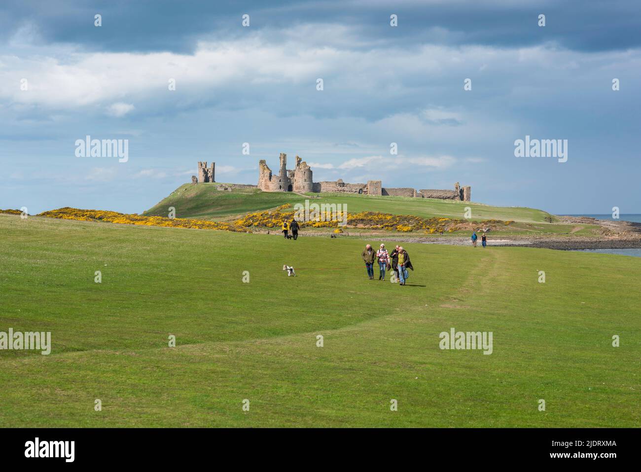 Senioren im Freien von Großbritannien, sehen Sie sich im späten Frühjahr eine Gruppe von Seniorenfreunden an, die den Northumberland Coast Path zwischen Craster und Dunstanburgh, Großbritannien, durchlaufen Stockfoto