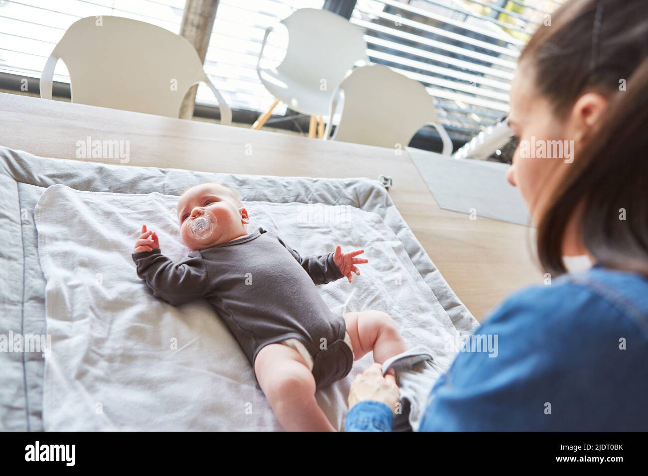 Baby ist in einem Strampelanzug auf dem Wickeltisch, nachdem die Mutter die Windel gewechselt hat Stockfoto