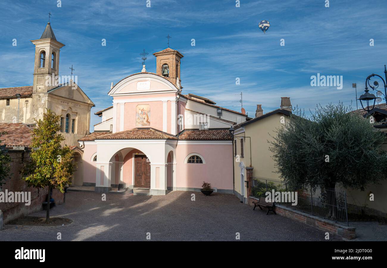 Die katholische Hauptkirche auf dem zentralen Platz von Barolo, Italien, mit einem Heißluftballon, der an einem Herbsttag in Piemonte, Italien, über dem Himmel fliegt Stockfoto
