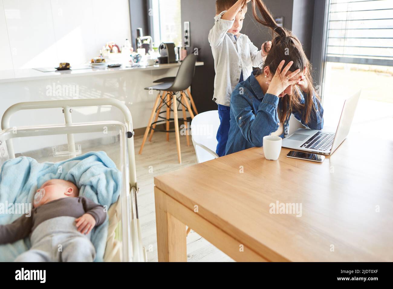 Alleinerziehende Mutter mit Burnout sitzt am PC im Heimbüro, gestört durch das Kind Stockfoto