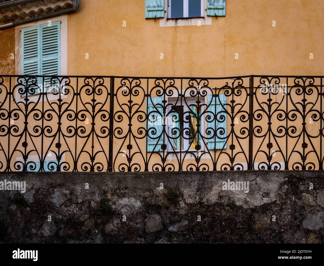 Abstraktes Muster, das von einem schmiedeeisernen Zaun mit einem alten Haus mit Fensterläden hinter ihm in einem provenzalischen Dorf im Südosten Frankreichs gebildet wurde. Stockfoto
