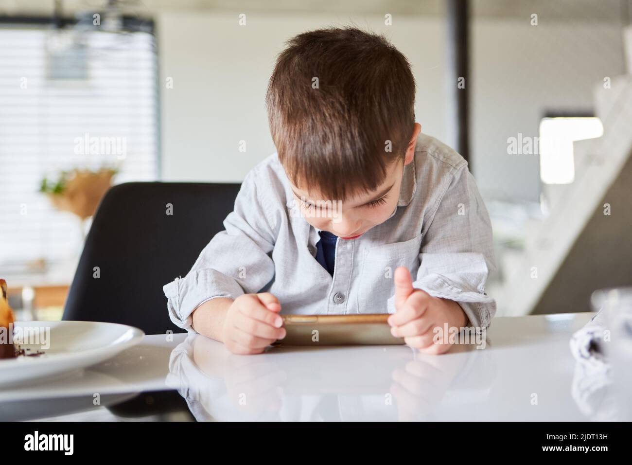 Der kleine Junge schaut aufmerksam auf sein Smartphone oder Tablet-Computer Stockfoto