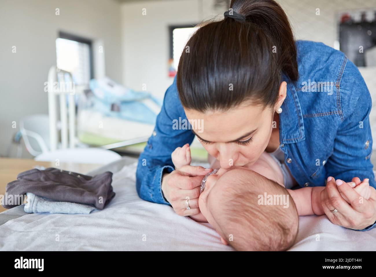 Glückliche Mutter gibt ihrem Baby einen Kuss, während sie die Windel auf dem Wickeltisch wechselt Stockfoto