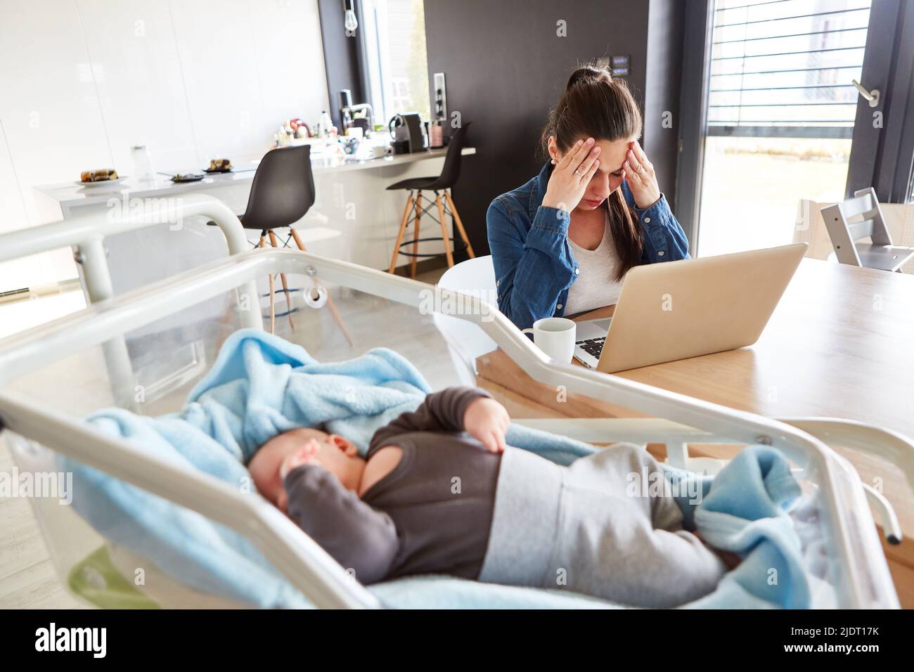 Erschöpfte alleinerziehende Mutter am pc im Heimbüro und schlafendes Baby im Vordergrund Stockfoto