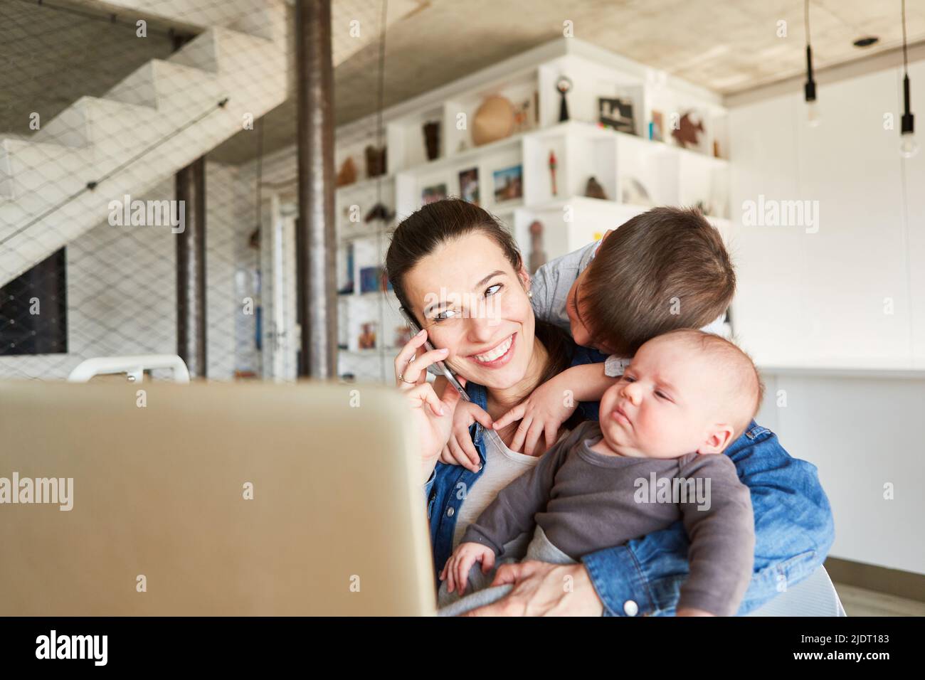 Die Mutter im Heimbüro telefoniert mit ihrem Smartphone und wird von Kindern abgelenkt Stockfoto