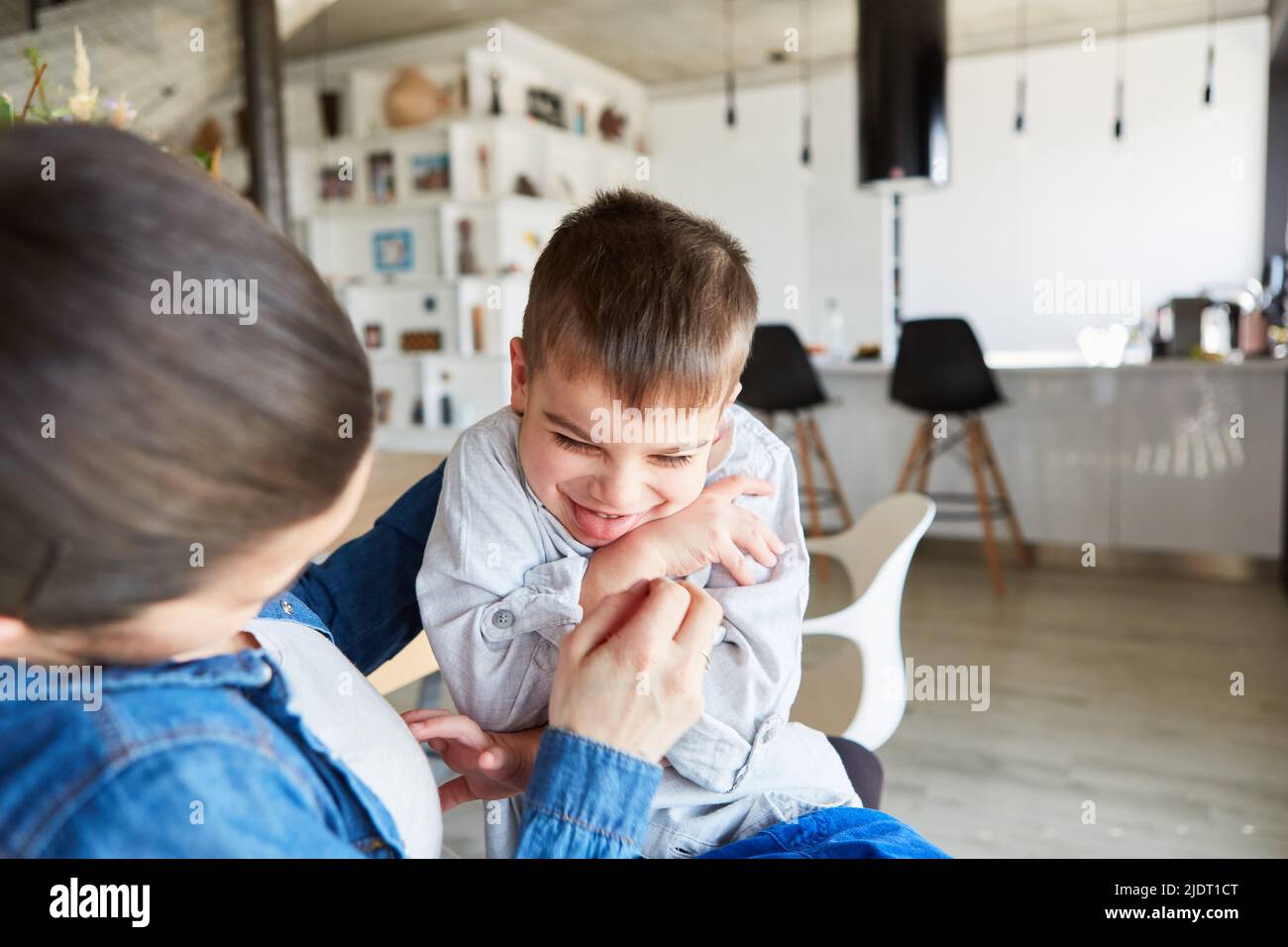 Mutter kitzelt ihren lachenden Sohn, während sie zu Hause im Wohnzimmer spielt Stockfoto