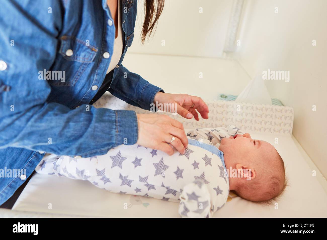 Das Baby im Schlafanzug auf dem Wickeltisch wird von der fürsorglichen Mutter betreut Stockfoto