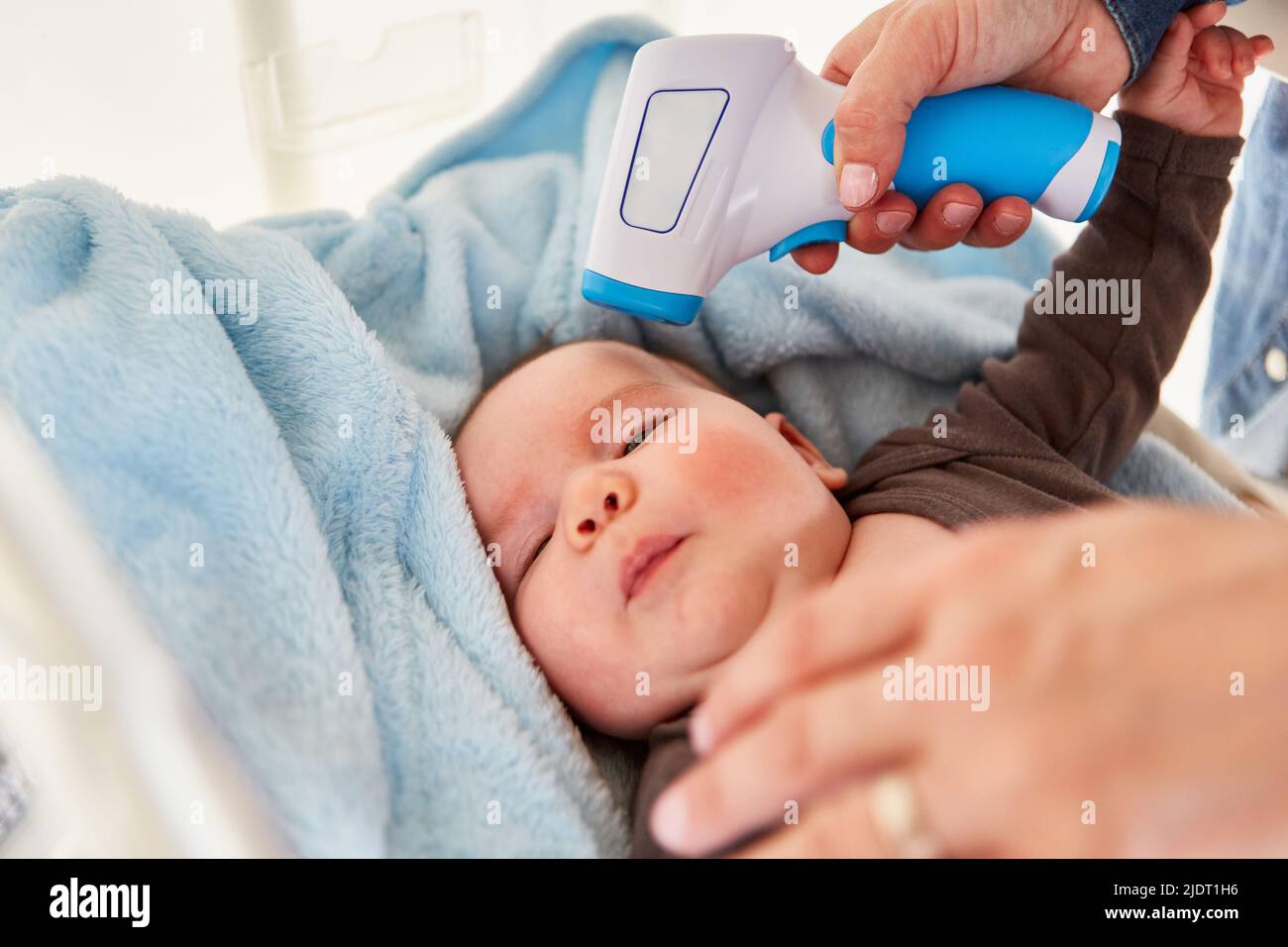 Mutter misst das kontaktlose Fieber des Babys auf der Stirn mit einem klinischen Thermometer Stockfoto