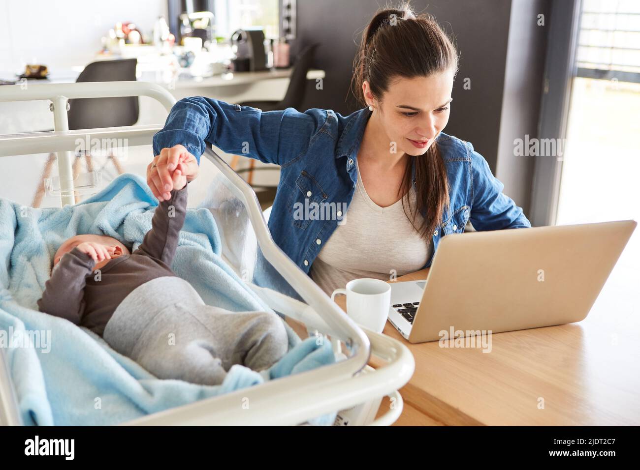 Mutter arbeitet am PC und kümmert sich im Nachbarbett um ihr Baby als Multitasking im Heimbüro Stockfoto