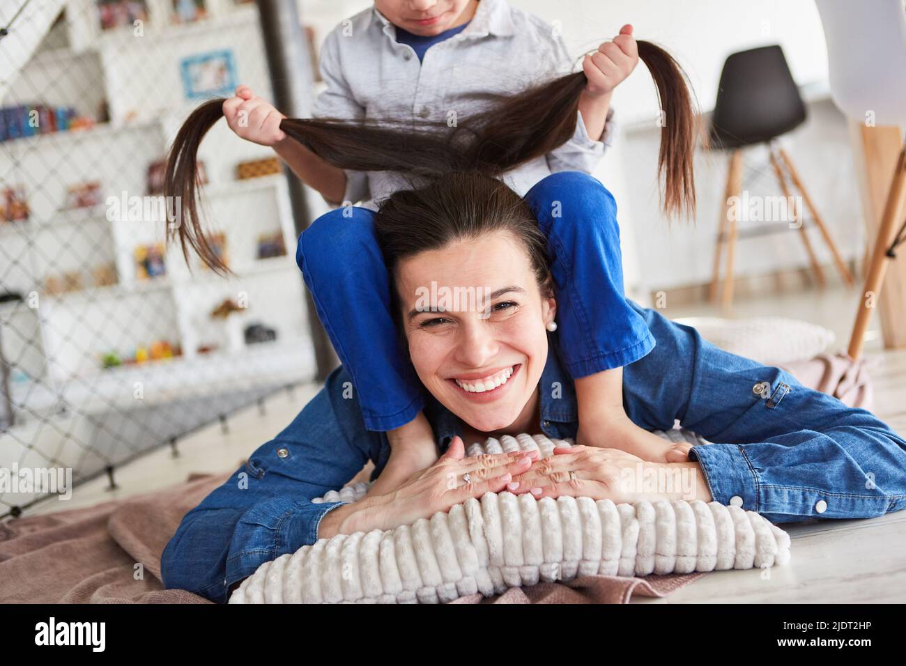 Glückliche Mutter, die auf dem Boden liegt und ihrem Sohn die Haare ziehen lässt Stockfoto