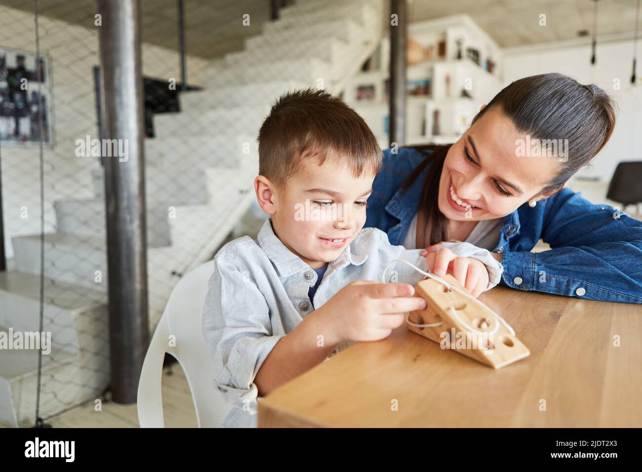 Junge, der mit seiner Mutter eine Schnur auf ein Holzspielzeug als Lernspiel einfädste Stockfoto