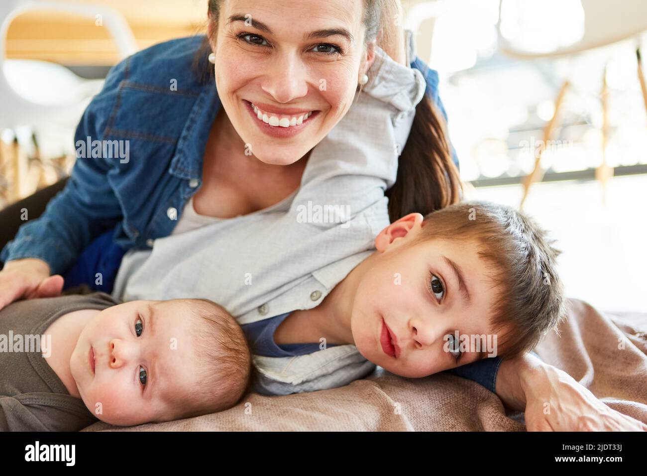 Glückliche Mutter kuschelt mit Baby und Kleinkind als großer Bruder zu Hause im Wohnzimmer Stockfoto
