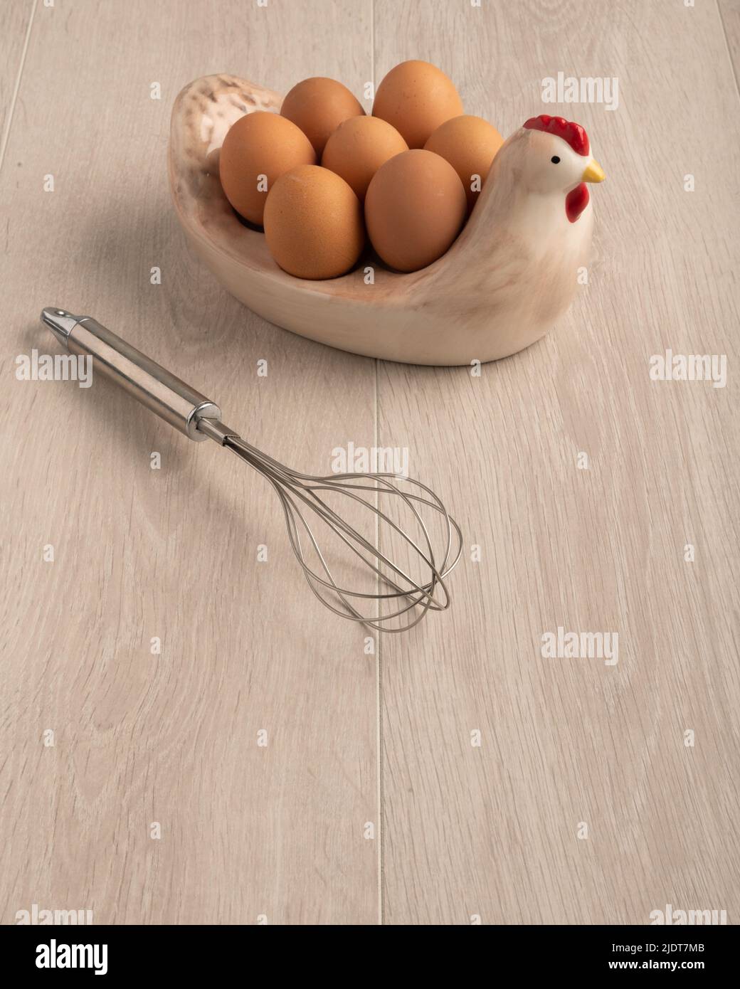 Ein Schneebesen Hühnereier in einer Glasschüssel und in einer Hühnerform auf einer hellen Holzoberfläche, mit negativem Platz zum Kopieren Stockfoto