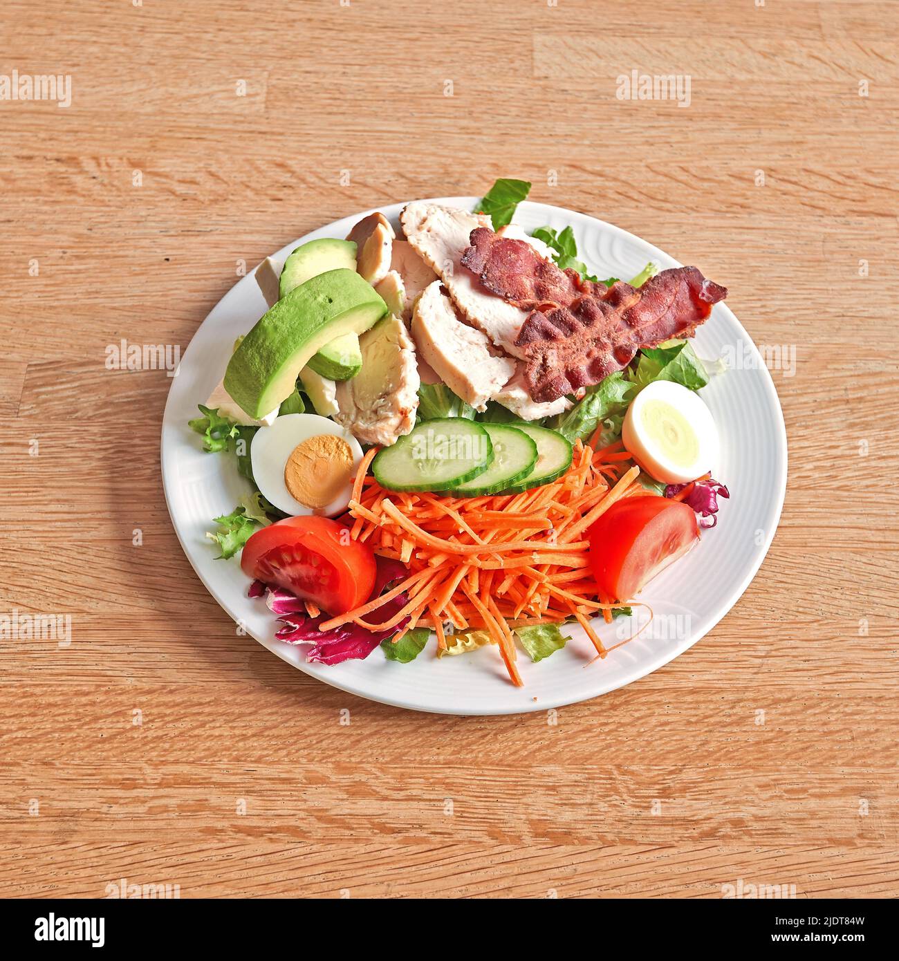 Weißer Teller mit Avocado und Fleischsalat auf Holztisch Stockfoto