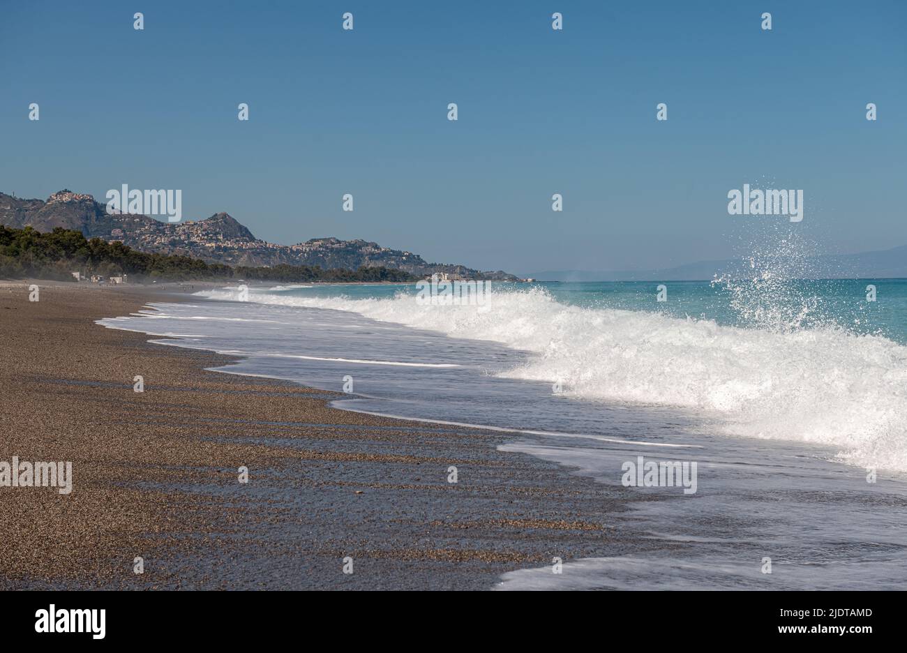 Brechende Wellen am schönen Strand von Fondachello, Sizilien, Italien. Die beliebten Städte Taormina und Giardini Naxos liegen in der Ferne Stockfoto
