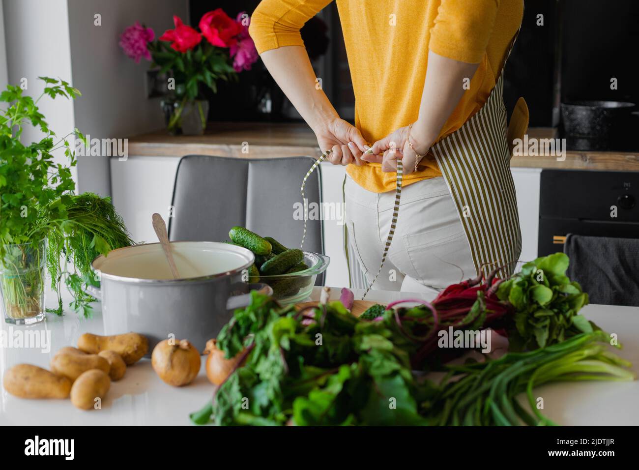 Nicht erkennbare Rückansicht Frau auf gestreifte Küchenschürze setzen, bereiten Sie sich für das Kochen Essen. Landwirtschaft Gemüsegericht Ernährung Stockfoto