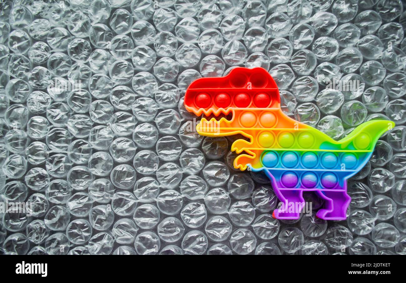 Spielzeug Pop it Dinosaurier Regenbogen Farben auf einem Luftpolsterfolie Hintergrund mit Platz für Text. Stockfoto