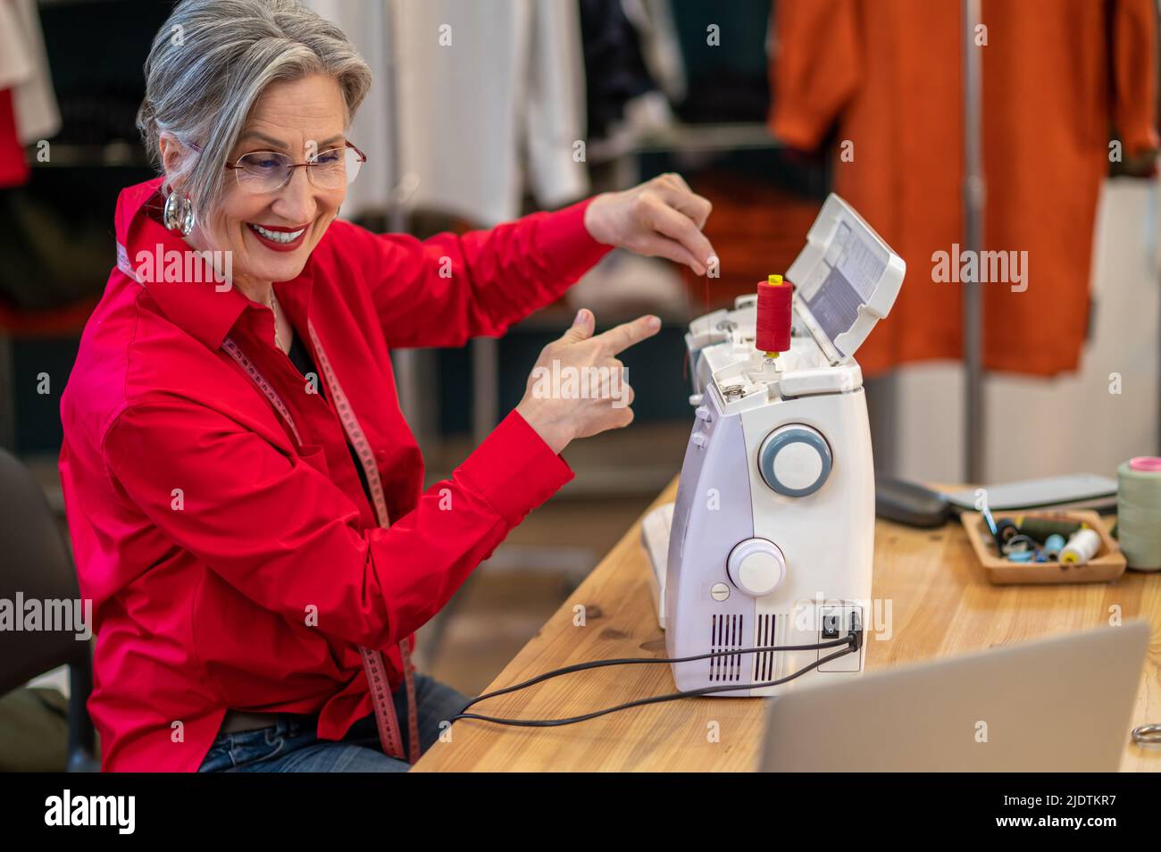 Frau, die auf den Faden zeigt, der in der Nähe der Nähmaschine sitzt Stockfoto