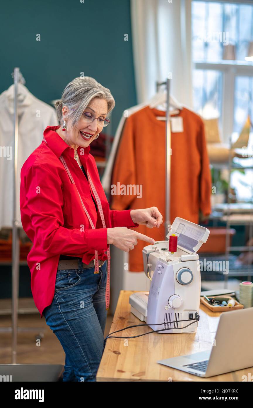 Frau in der Nähe der Nähmaschine, die in den Laptop spricht Stockfoto