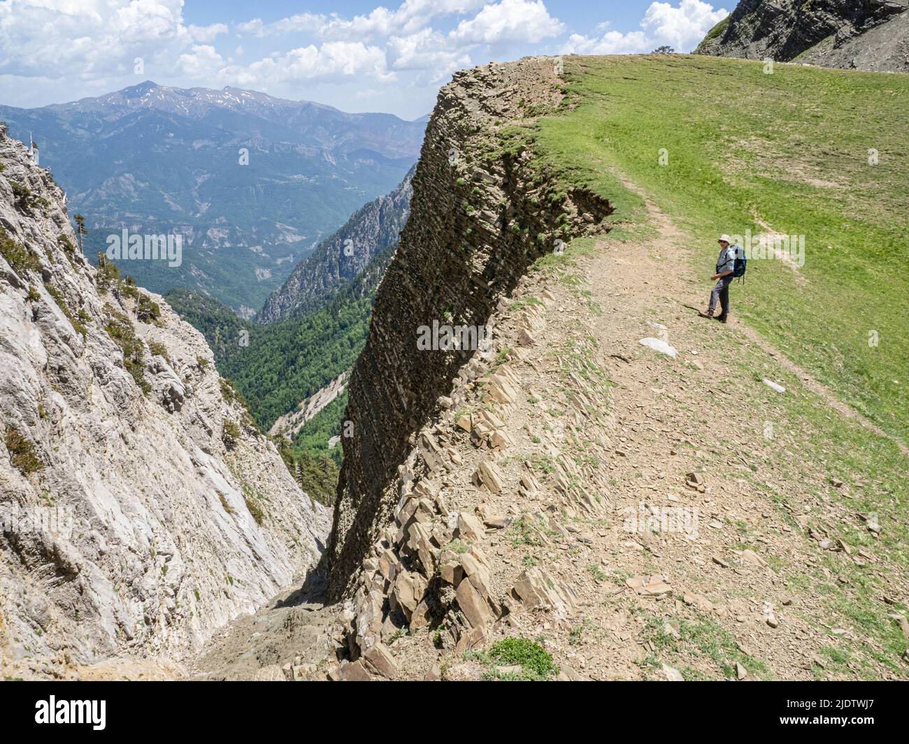 Ein Spaziergänger am Abgrund jenseits von Drakolimni der Drachensee auf dem Berg Timfi in den Pindus Bergen von Griechenland mit Blick auf den Berg Trapeziza Stockfoto