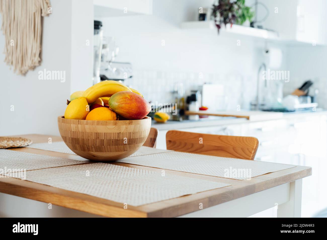 Hauptküche Counter Tisch mit selektivem Fokus auf Bambus Schüssel mit exotischen Früchten auf sie mit verschwommenem Hintergrund der modernen gemütlichen weißen Küche. Home int Stockfoto