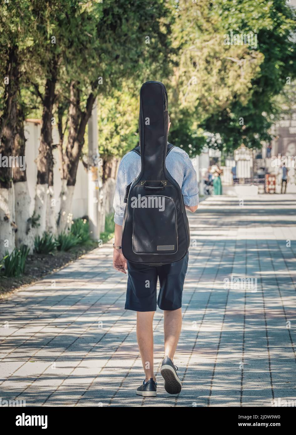 Rückansicht eines Mannes, der mit einem Gitarrenkoffer auf dem Rücken läuft Stockfoto