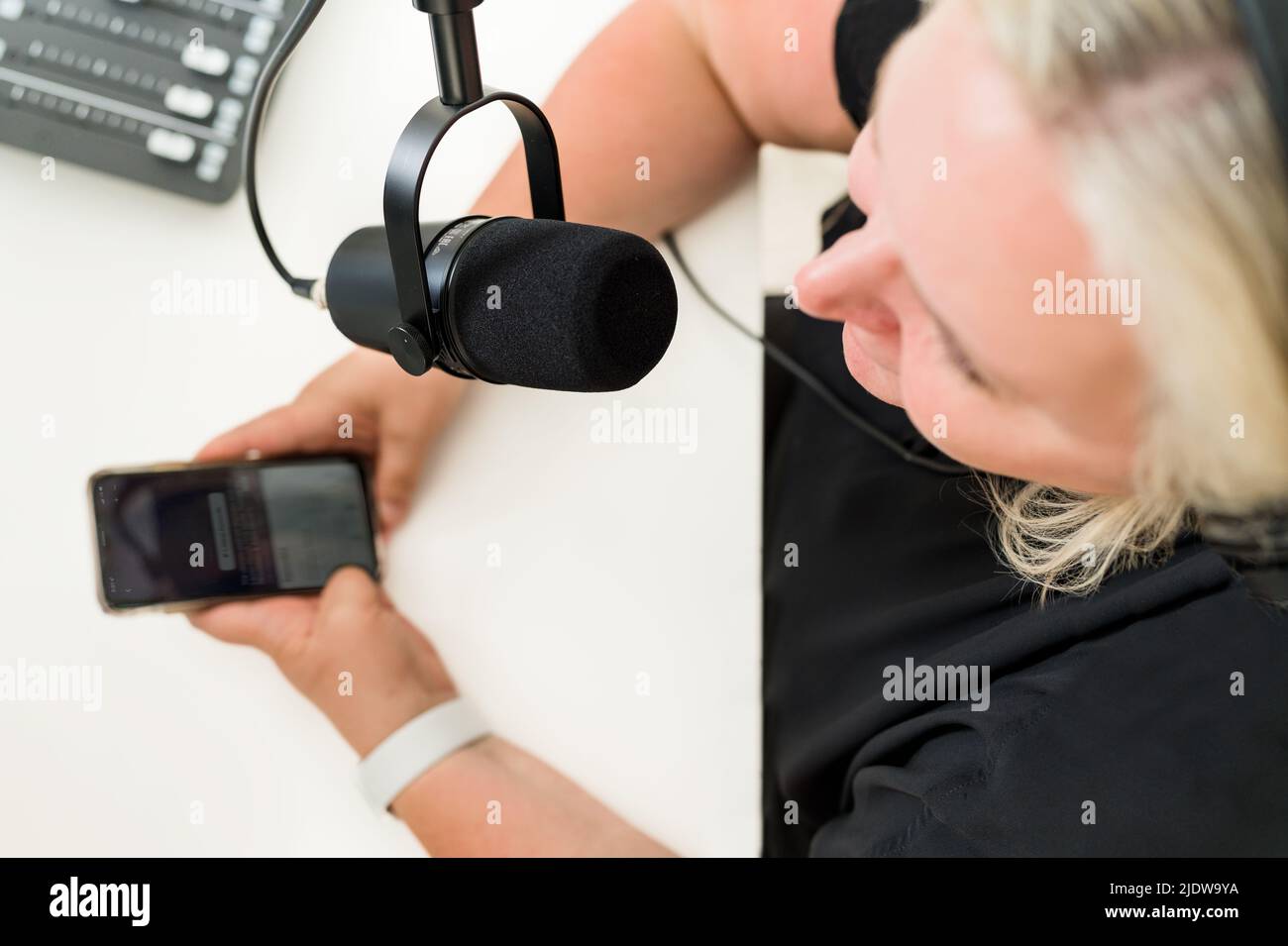 Frau von oben vor dem Mikrofon mit Telefon in den Händen und Klangmischpult Stockfoto